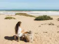 Kobieta pije herbatę na plaży, delektując się widokiem na wzburzone morze. To właśnie takie morze można podziwiać w Tunezji.
