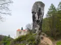 Skała z krzyżem i zamek na wzgórzu w krajobrazie Jury Krakowsko-Częstochowskiej.