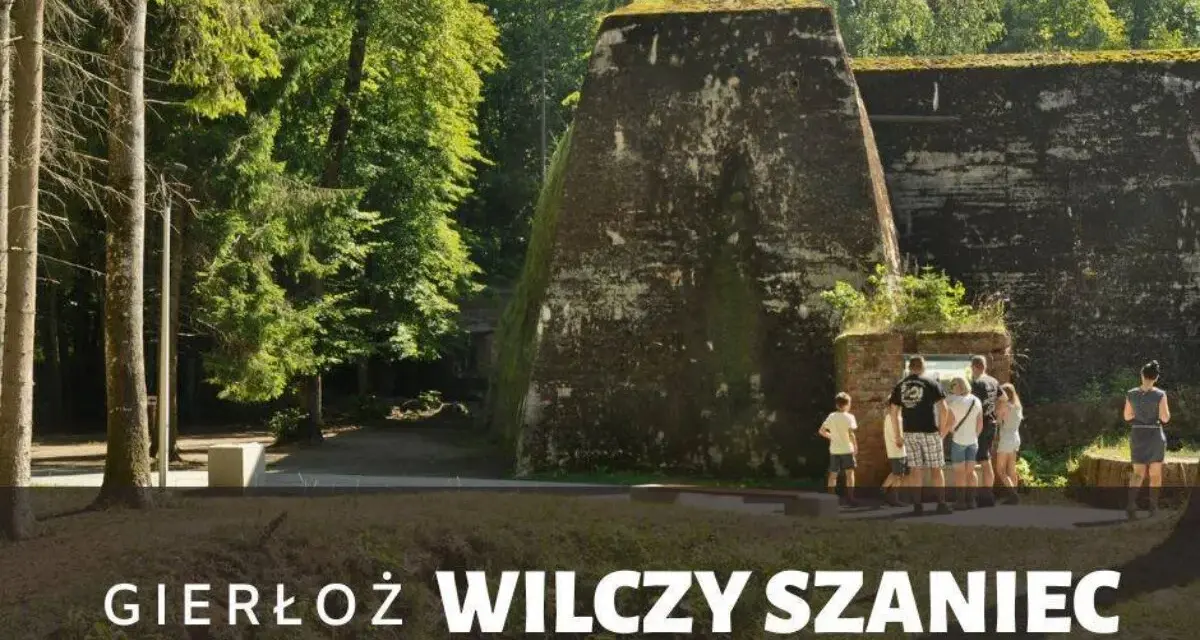 Grupa turystów zwiedza historyczny Wilczy Szaniec, otoczony bujną zielenią.
