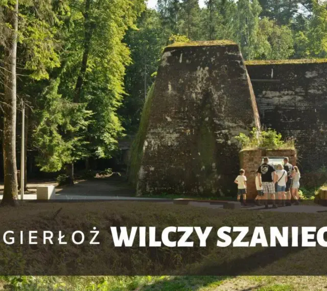 Grupa turystów zwiedza historyczny Wilczy Szaniec, otoczony bujną zielenią.