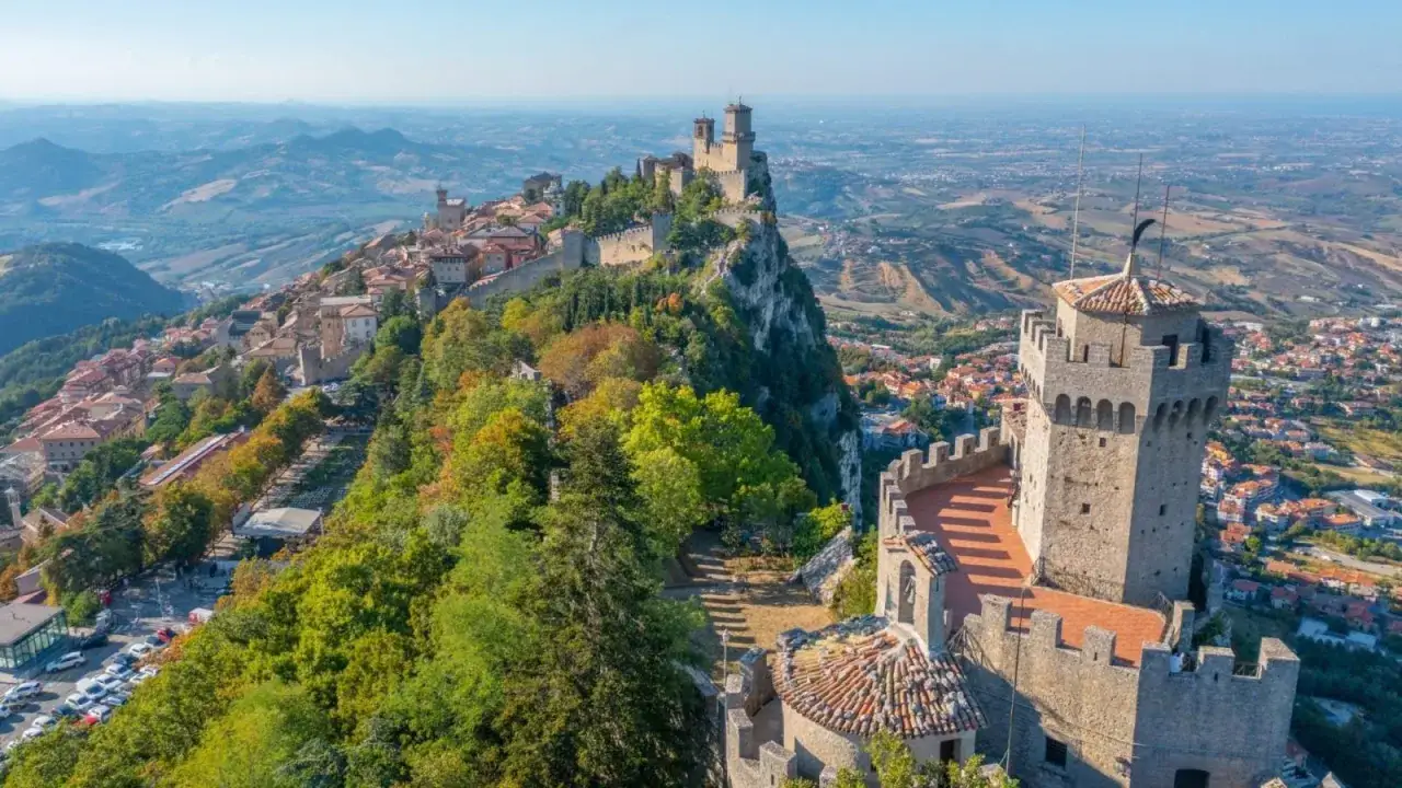 Trzy wieże obronne górują nad wzgórzem w San Marino, otoczone zielenią i zabudowaniami.