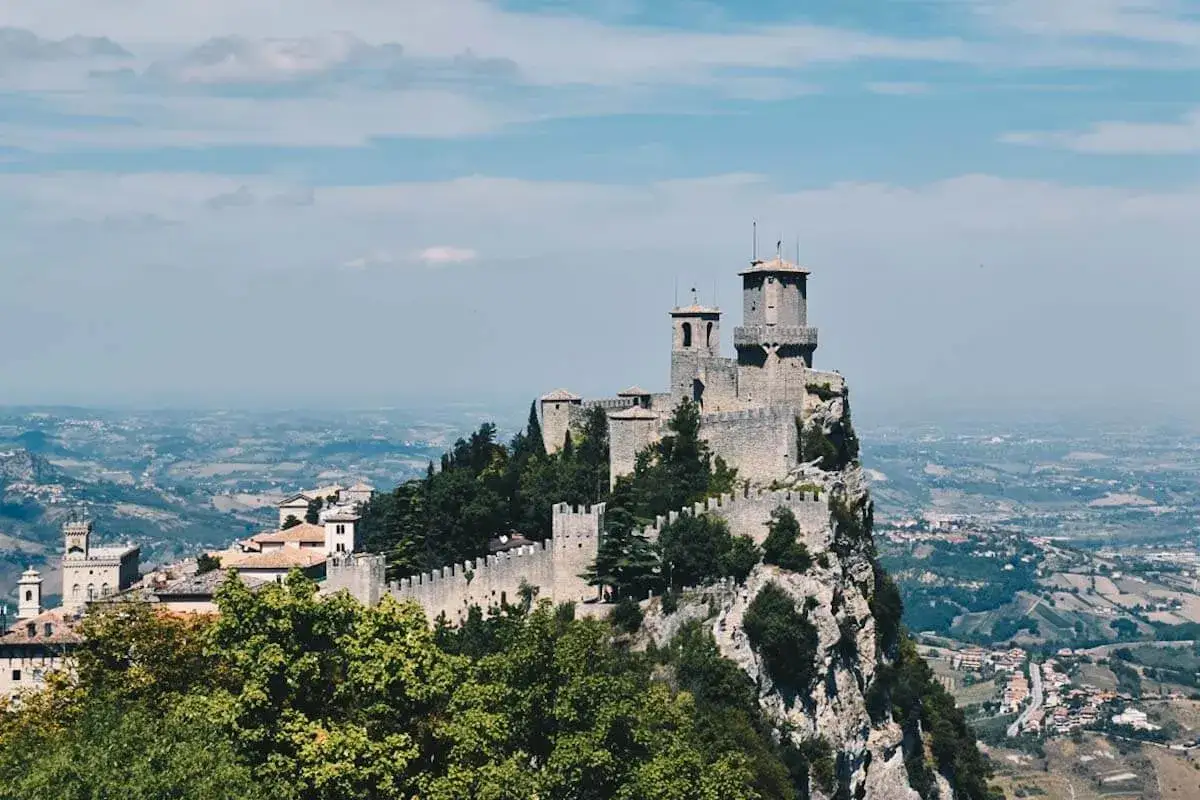 Trzy wieże obronne górują nad skalistym szczytem w San Marino, otoczone zielenią i rozległym krajobrazem.